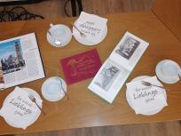 Auf einem Tisch liegen unterschiedliche Flyer, Bilder , die zum Thema der Seniorengruppe passen. Ein paar Kaffeetassengehören ebenfalls dazu.